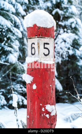 Old weathered kilomètre en bois rouge signe avec la neige sur la route forestière Banque D'Images