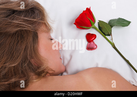 Une femme est en train de dormir alors qu'une rose rouge et chocolats en forme coeur ont été laissé sur son oreiller pour la Saint-Valentin. Banque D'Images