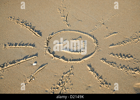 Peinture à la main d'un soleil souriant symbole dans le sable d'une plage. Banque D'Images