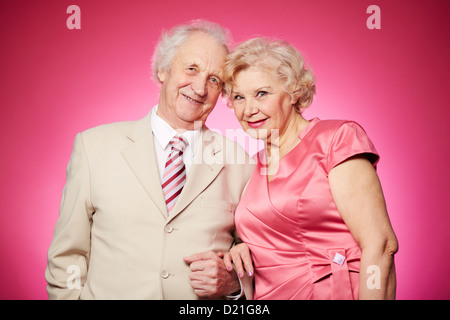 Portrait d'un charmant couple de retraités posant contre fond rose Banque D'Images