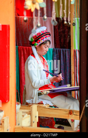 Portrait d'une femme traditionnelle Bai tissage, reflétée dans le miroir de sa boutique à Dali, Yunnan, sud-ouest de la Chine. Banque D'Images