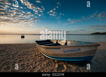 Bateau abandonné sur une plage de sable à un lac au lever du soleil Banque D'Images