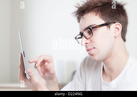 Jeune homme portant des lunettes à la recherche à l'écran de sa tablette numérique. Banque D'Images