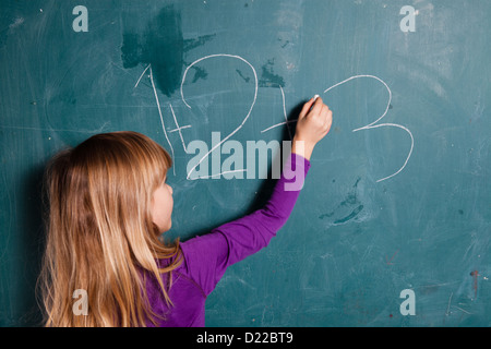 Jeune fille l'écriture des chiffres sur le tableau avec de la craie Banque D'Images