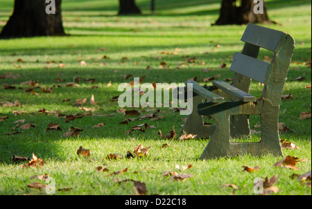 Banc en bois vide sur l'herbe vert vif parsemé de feuilles d'Or Banque D'Images