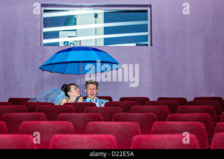 Jeune couple assis sous un parapluie dans cinéma le jour de leur mariage Banque D'Images