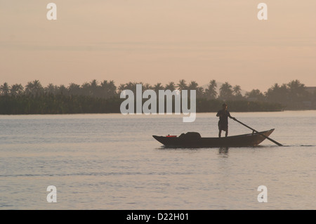 Comme le lever du soleil se brise sur la rivière, un pêcheur solitaire oriente son bateau pour vérifier ses filets de pêche à Hoi An Vietnam Banque D'Images