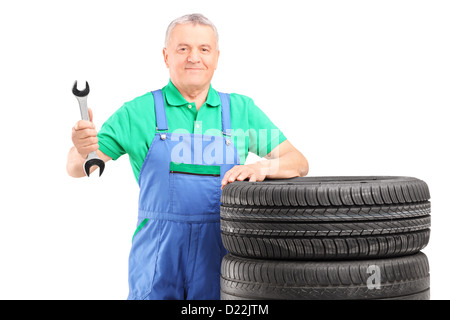Mécanicien matures debout avec les pneus de voiture et tenant une clé dynamométrique isolé sur fond blanc Banque D'Images