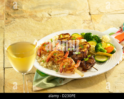 Boeuf et crevettes brochettes de poulet servi sur du riz pilaf aux légumes mixtes et un verre de vin blanc Banque D'Images
