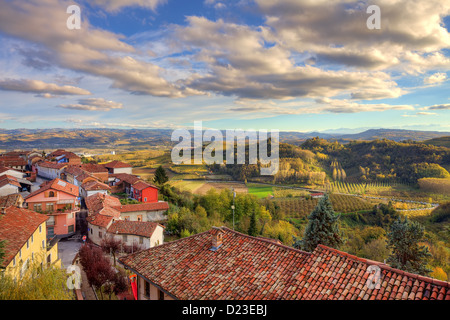 Vue sur les toits rouges de petite ville entre les collines et les prairies sous ciel magnifique au coucher du soleil en automne en Piémont, Italie. Banque D'Images