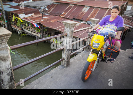 13 janvier 2013 - Bangkok, Thaïlande - une femme rides son scooter à Khlong Bang Luang à Bangkok. Le quartier de Khlong Bang Luang lignes (Canal) Bang Luang dans la section de Thonburi Bangkok sur le côté ouest de la rivière Chao Phraya. Il a été établi à la fin du xviiie siècle par le roi Taksin le grand après les Birmans à sac la capitale Siamoise d'Ayutthaya. Le quartier, comme la plupart de Thonburi, est relativement peu développé et criss encore traversé par les canaux qui ont fait de Bangkok célèbre. C'est maintenant une promenade journalière du centre de Bangkok et offre un aperçu de ce que la ville utilisée pour Banque D'Images