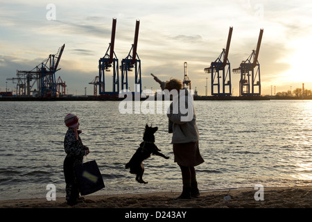 Une mère et sa fille, rendant leur chien jump en face du Terminal Burchardkai dans la soirée, le port de Hambourg, Allemagne Banque D'Images