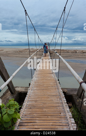 Les hommes marcher sur pont suspendu au-dessus de petite rivière menant à la mer de Bali. Banque D'Images