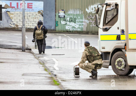 Belfast, en Irlande du Nord, Royaume-Uni. 14 janvier 2013. L'Escadron 321 de l'armée de l'ATO, 11 Régiment de NEM, vêtu d'un costume à l'épreuve des bombes s'approche d'un dispositif suspect portant une explosion contrôlée 'pig stick". Son collègue est titulaire d'une bobine de câble de l'explosion. Banque D'Images