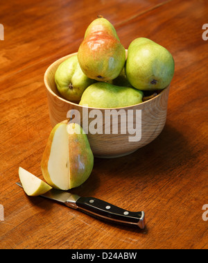 Poires Bartlett fraîches dans un bol en bois sur une table avec une coupe par couteau à légumes Banque D'Images