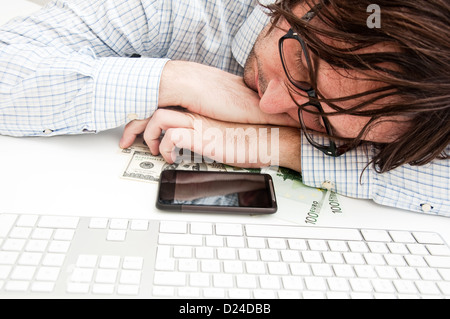 Homme laborieux s'endormir au bureau, son téléphone portable et un peu d'argent en face de lui. Banque D'Images