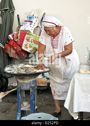 Vieille Femme immaculée vendeur ajoute une chaîne à Oaxaca fromage tacos cuisiner à l'extérieur sur trottoir cuisinière Oaxaca de Juarez, Mexique Banque D'Images