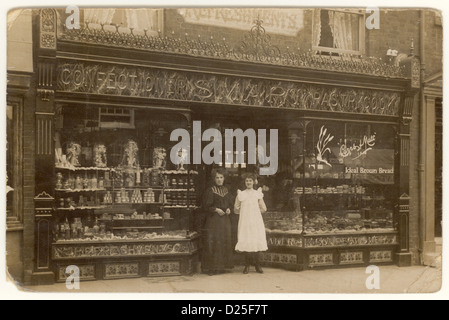 Carte postale édouardienne originale de pâtisseries, confiseries, bonbons sucrés et boulangers magasin appelé 'Smart Pastry Cook' - propriétaire / propriétaire et assistant / personnel femme à l'extérieur, produits affichés dans la vitrine des devantures du magasin. Magasins victoriens. Daté de 1909, Southampton, Hampshire, Angleterre, Royaume-Uni Banque D'Images