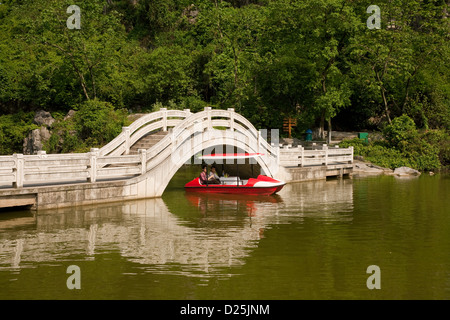 Un pédalo passe sous un pont sur l'ouest du lac dans le parc Xishan dans le sud de la Chine. Banque D'Images