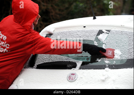 Brighton Sussex UK 14 Janvier 2013 - Jeune femme portant un Cœur rouge veste radio racler la glace et neige sur un Cinquicento Fiat Banque D'Images