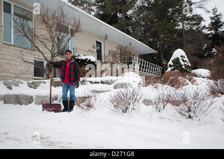 Un jeune Indien de l'homme à la pelle la neige devant sa maison Banque D'Images