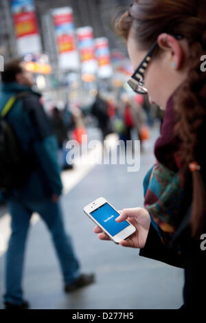 Une jeune femme appelle le réseau facebook sur son téléphone portable à l'intérieur d'une foule de gens. Banque D'Images