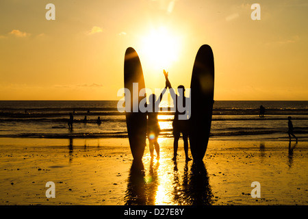 Couple surfeur en silhouette tenant longtemps des planches de surf au coucher du soleil on tropical beach Banque D'Images