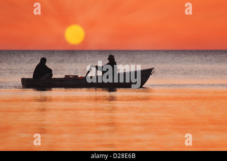 Deux silhouettes d'hommes dans un bateau de pêche au coucher du soleil Banque D'Images