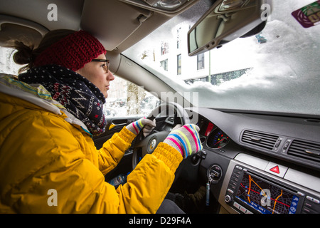 Une voiture est couverte de neige et de glace. Femme essaie de conduire la voiture, avec juste un trou dans le pare-brise, couverte de neige. Banque D'Images