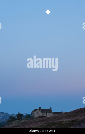 Pleine lune au crépuscule, haut dans un ciel bleu au-dessus sur une maison en pierre sur la lande de bruyère - au-dessus de Burley-en-Wharfedale, West Yorkshire, Angleterre, Royaume-Uni. Banque D'Images