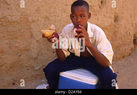 Un jeune garçon djablani vente verre au Mali, Afrique de l'Ouest. Les petits sacs en polyéthylène de jus aromatisé avec le bissap (rouge) ou le gingembre Banque D'Images