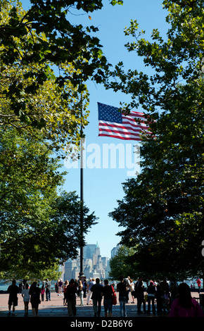 US flag vu entre les arbres sur Liberty Island avec la partie basse de Manhattan au loin. Banque D'Images