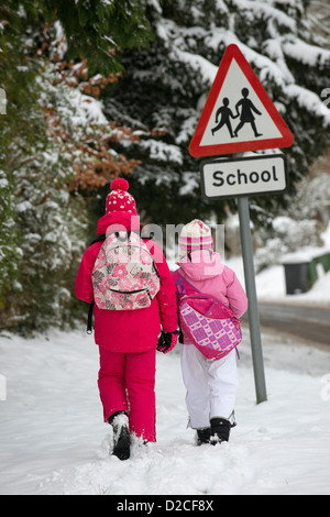 Enfants à l'école à pied le long d'une route couverte de neige avec un signe de l'école Banque D'Images