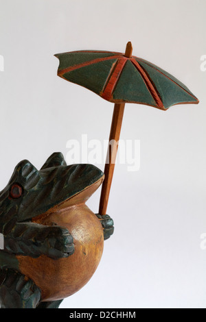 Grenouille en bois holding an umbrella situé sur fond blanc Banque D'Images