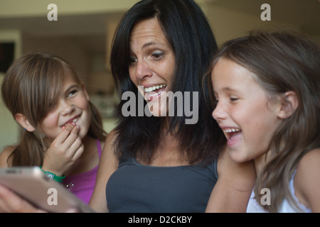 Mère et ses deux filles à regarder quelque chose de drôle sur un ipad. Fille cherche à voir la réaction de maman. Banque D'Images