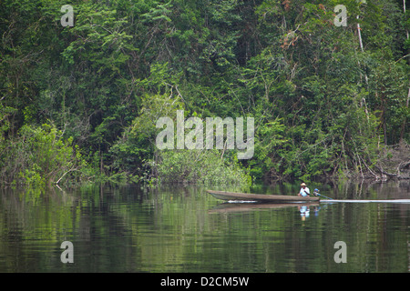 Pêcheur local voyage en canoë en bois le long des eaux calmes de la rivière Amazone, au Brésil, entouré d'une forêt tropicale dense Banque D'Images