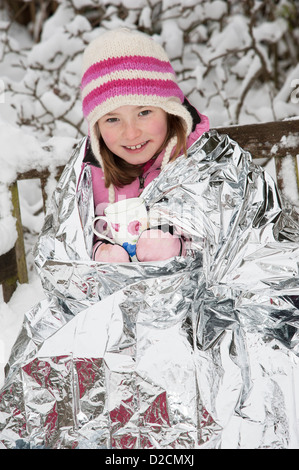 Jeune fille à l'aide d'une feuille de couverture pour garder la chaleur et empêcher le froid de l'hiver tout en appréciant une boisson chaude Banque D'Images