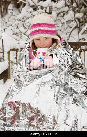 Jeune fille à l'aide d'une feuille de couverture pour garder la chaleur et empêcher le froid de l'hiver tout en appréciant une boisson chaude Banque D'Images