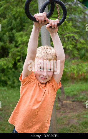 Jeune garçon exerçant sur les anneaux de gymnastique en plein air Banque D'Images