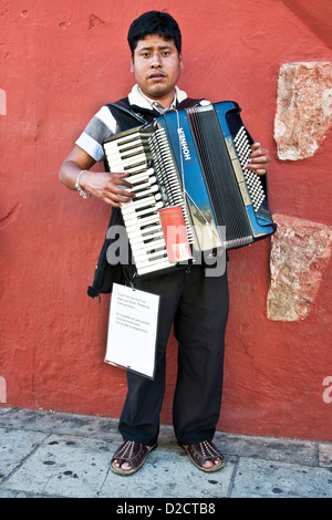 Jeune mexicaine aveugle homme debout à l'extérieur en rue en face du magnifique mur rouge jouant son accordéon Oaxaca de Juarez, Mexique Banque D'Images