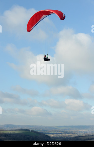 Un homme vole en parapente sur le Sud des bas dans le West Sussex avec une chute rouge sur un beau jour avec ciel bleu et nuages blancs Banque D'Images