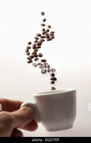 Un homme tenant une tasse de café avec café en grains flottant au-dessus Banque D'Images