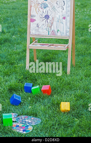 Un chevalet, des blocs de jouets et les peintures à l'aquarelle dans l'herbe d'un jardin Banque D'Images