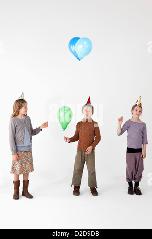 Trois kids wearing party hats et holding balloons Banque D'Images