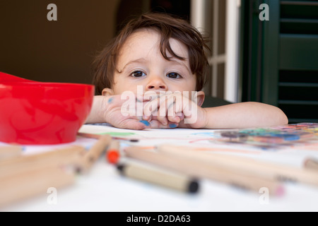 Un enfant s'appuyant sur une table jonchée de crayons de couleur et des fournitures artistiques Banque D'Images