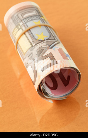 50 Euro note sur un rouleau de Euros roulées avec une bande élastique sur un fond d'or orange clair. L'UE l'Europe Banque D'Images
