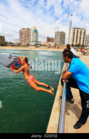 Durban, Afrique du Sud. Une jeune femme sort de l'internaute la jetée dans l'océan sur la plage de Durban, regardée par les passants. Durban, Afrique du Sud. Banque D'Images