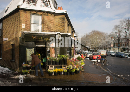 Employé d'Bartleys le fleuriste entreprise en 76200 Village, South London, brosses, la fonte de la neige de la chaussée. Banque D'Images