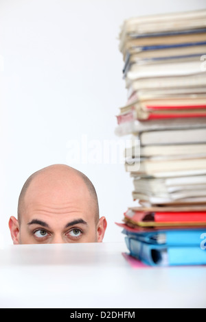 L'homme se cachant derrière un bureau à regarder une pile de livres Banque D'Images