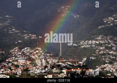 Un arc-en-ciel au-dessus de Funchal à Madère avec la route côtière principale en arrière-plan sur un pont haut. Banque D'Images